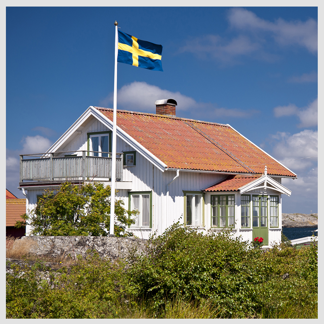 Flaggstång med svensk flagga utanför hus vid kusten