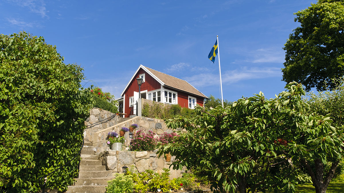 Flaggstång med svensk flagga vid rött hus i sommarmiljö